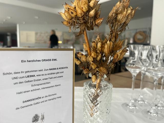 Kleine Vase mit getrockneten Enzianblüten, Austeller mit Einladungstext.