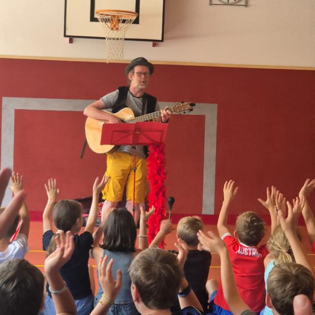 Musiker Konrad Bönig mit Gitarre vor den zuhörenden Kindern.