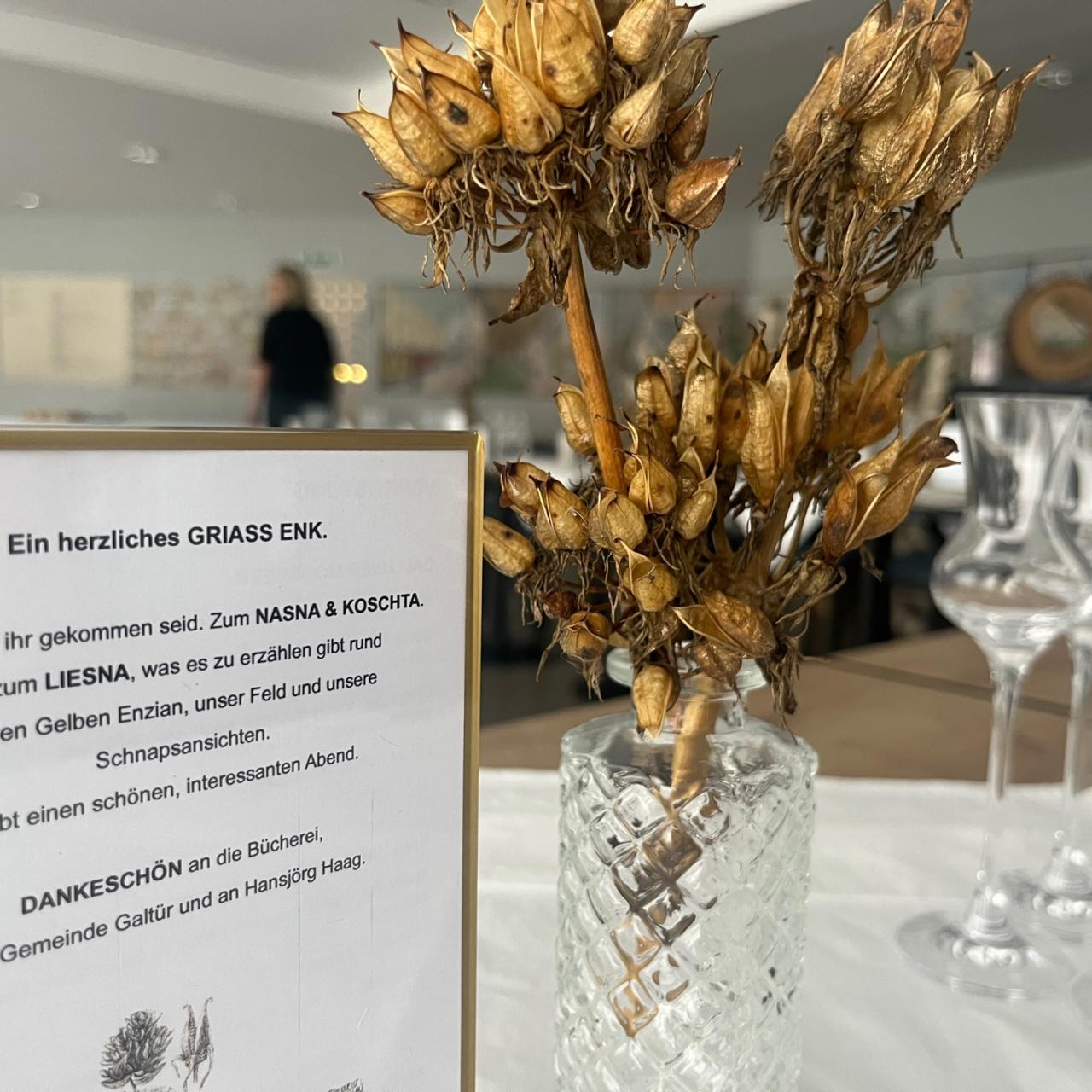 Kleine Vase mit getrockneten Enzianblüten, Austeller mit Einladungstext.